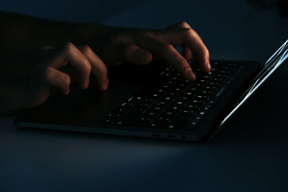 Hands typing on a backlit laptop keyboard in a dim room